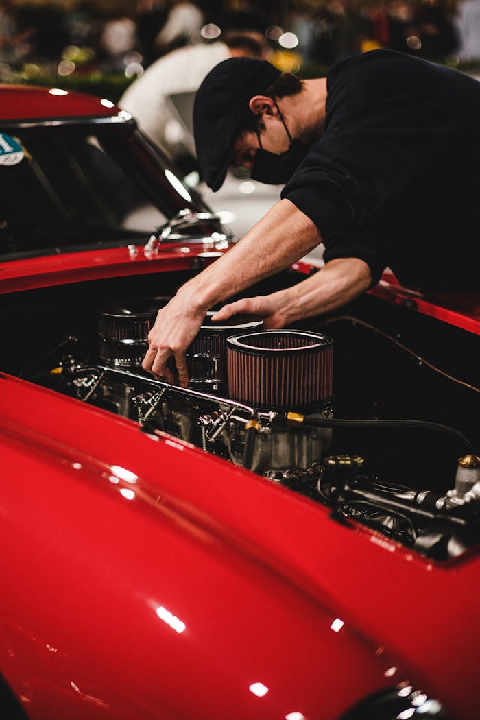 Close-up of a mechanic tuning a classic car engine in an indoor garage setting.